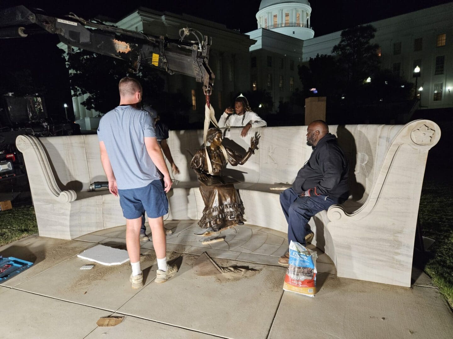 Two men lowering a bronze figure into the centre of a marble memorial at night