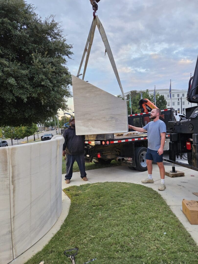 Crane lifting a large marble panel off a flatbed trailer