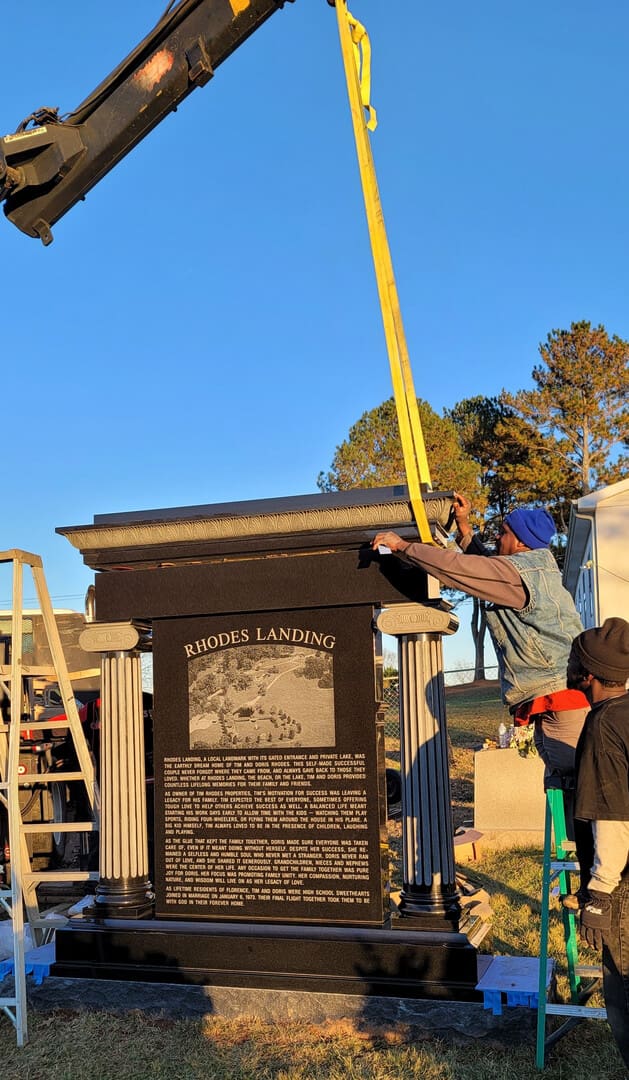A civic monument being lowered onto its base by crane at dusk