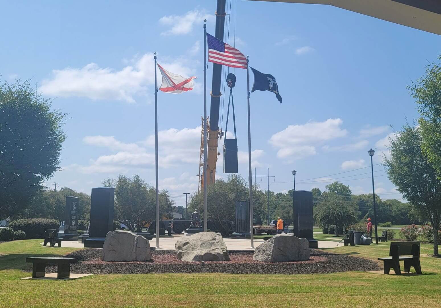 Memorial park with United States and Alabama flags flying and a crane at work among the stones
