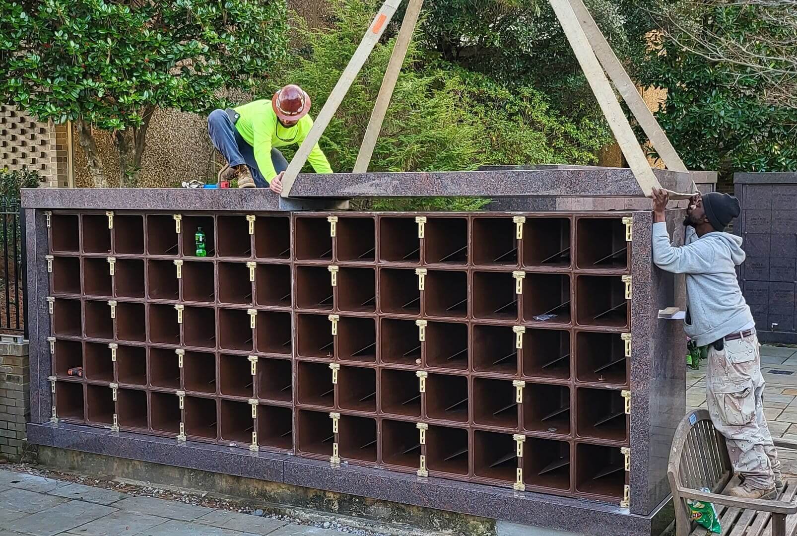 Two men fitting the timber frame of a columbarium with its niches open