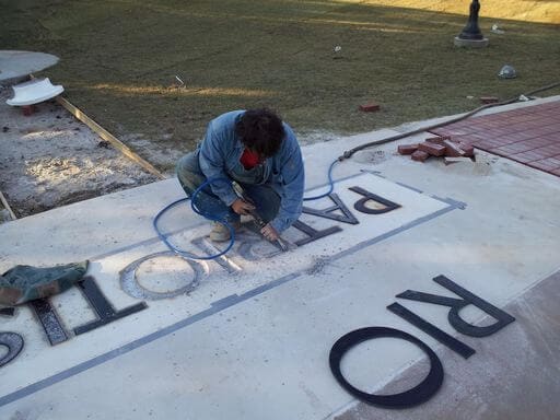 A man kneeling to cut the word PATRIOTISM into a pale memorial paving stone