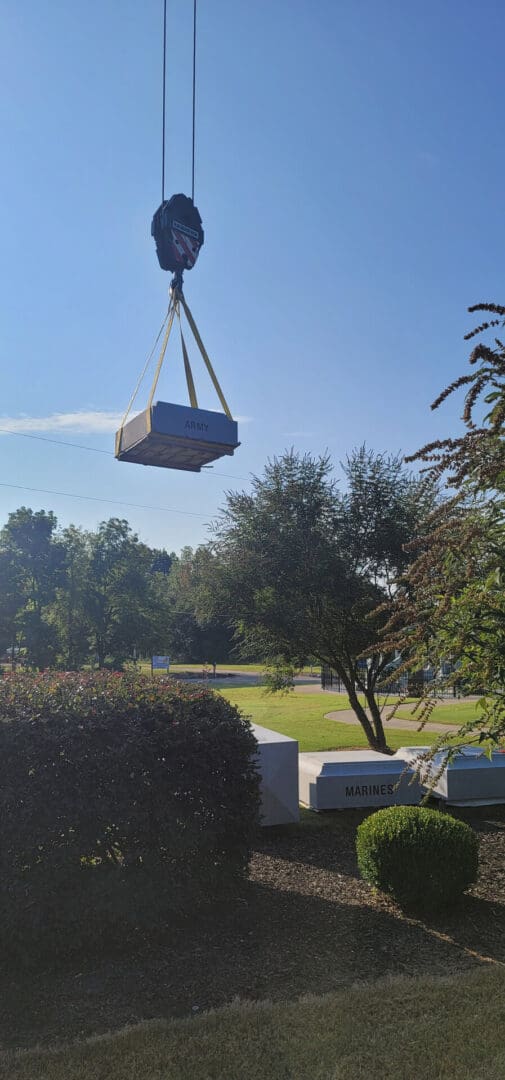 A crane lowering a monument over a hedge into a cemetery