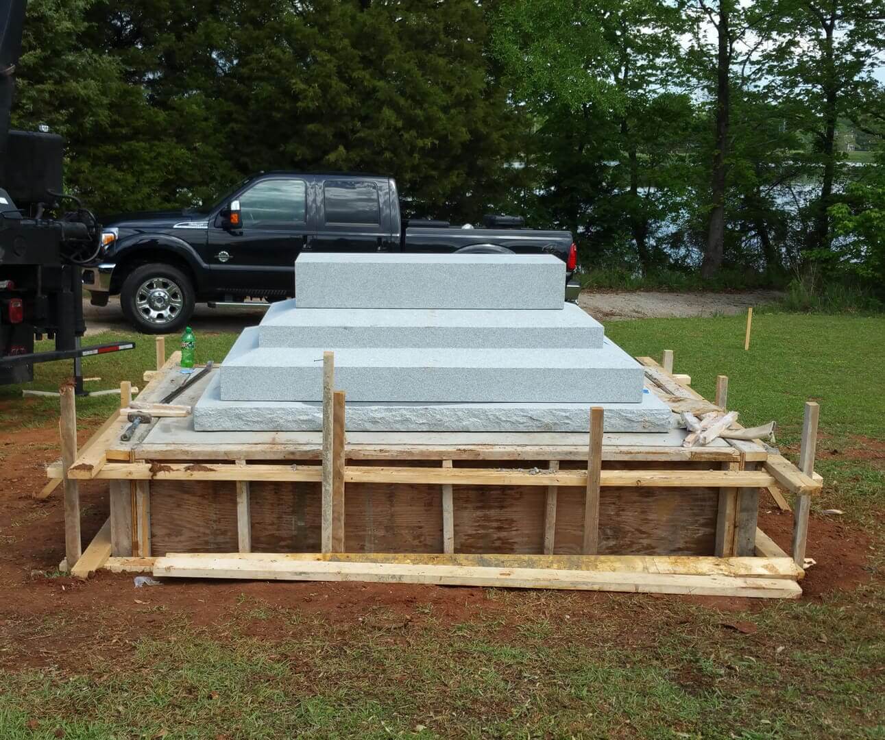 A long timber-formed concrete foundation poured in a cemetery with a truck alongside