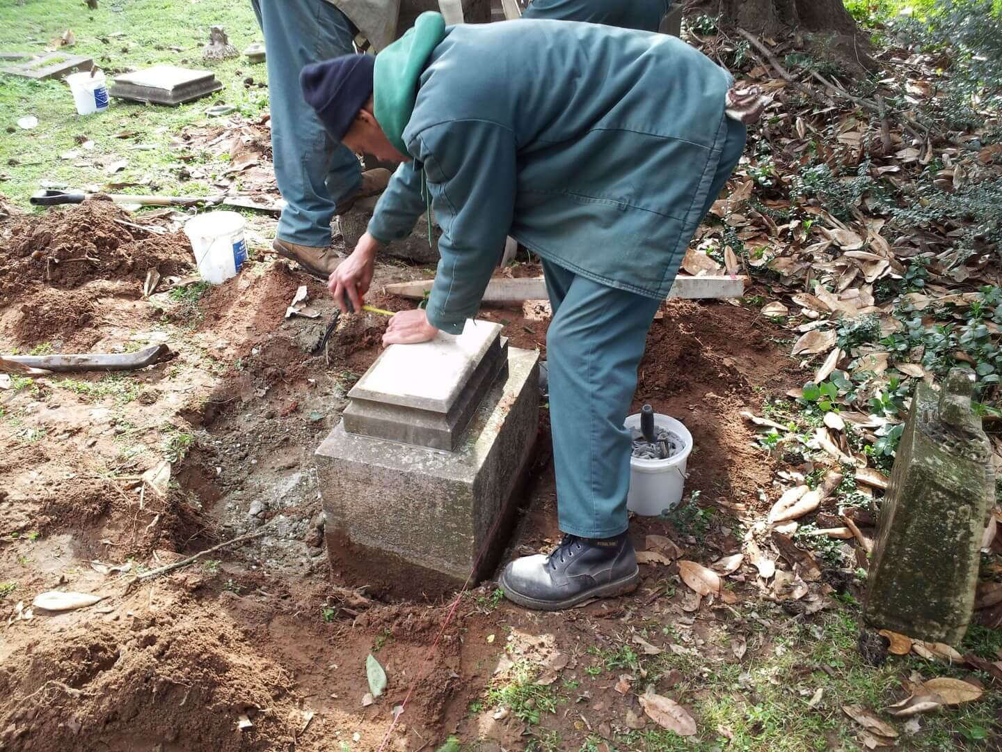 Two men kneeling to hand-set a marker base into an excavated foundation