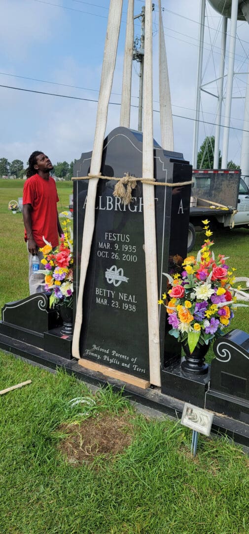 A black granite upright monument standing on its base in a cemetery with the hoist frame still around it