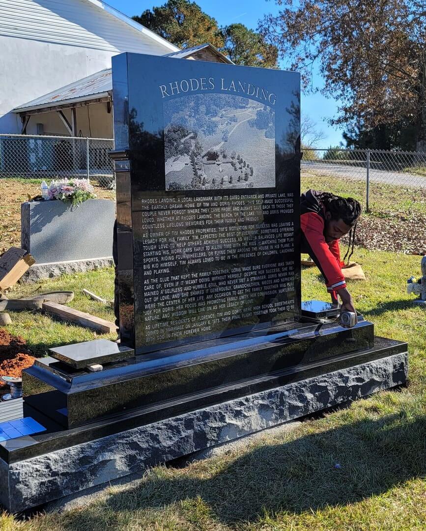 Black granite civic monument with an etched scene and a long inscription, standing on a rough stone base