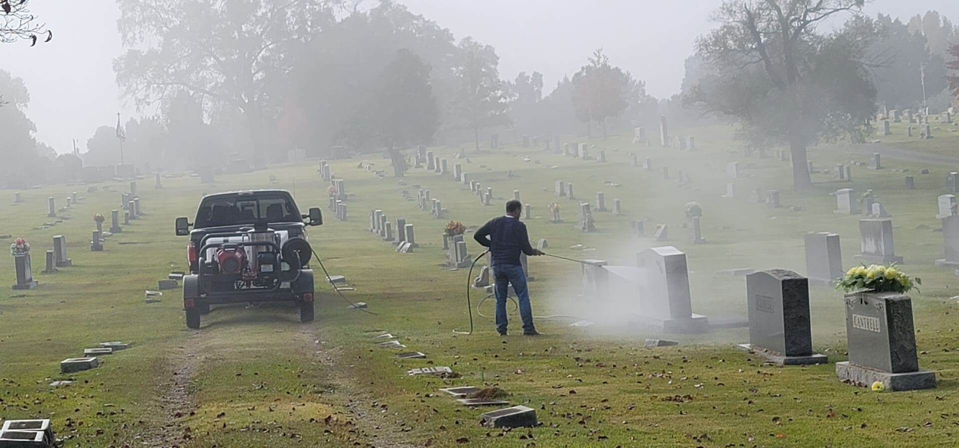 Monument cleaning in progress across a foggy cemetery, spray drifting between the stones